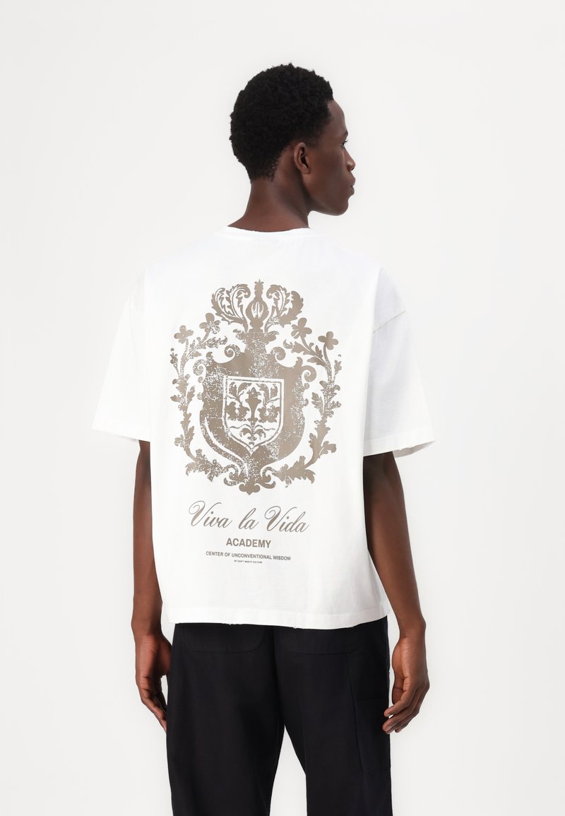 White short-sleeve t-shirt featuring a large, detailed gold graphic print on the back, including text and ornate design elements.