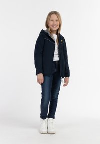 Mornarska zip-up jakna s sivo kapuco, z belimi detajli, v kombinaciji z modrimi kavbojkami in belimi visokimi supergami.