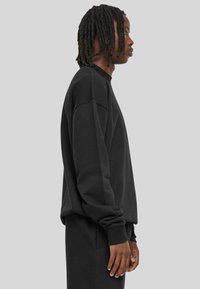 Sweatshirt noir à col rond avec des poignets et un ourlet côtelés. Fabriqué en tissu doux et texturé, il présente une coupe décontractée et des épaules tombantes.