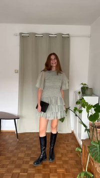 Lysegrønn lagdelt kjole med teksturert stoff, korte puffermer, kombinert med høye svarte støvler og en svart clutch. Innendørs setting.