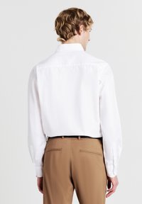 Weißes Langarmhemd mit Standardkragen und Knopfmanschetten, kombiniert mit beigefarbenen Hosen mit glatter Textur und Gesäßtaschen.