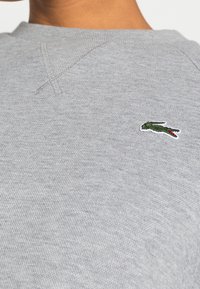 Grå bomullströja med strukturerad yta, med en liten broderad grön och röd krokodil-logotyp på vänster bröst.