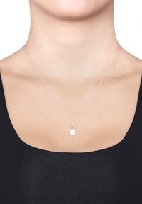 Silberne Kettenhalskette mit einem tropfenförmigen weißen Anhänger, der eine strukturierte Oberfläche und dekorative Details in der Nähe des Verschlusses aufweist.