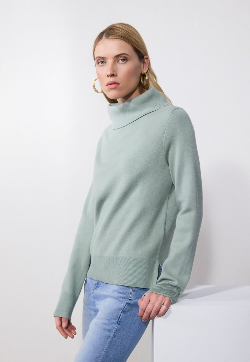 Light green turtleneck sweater in a soft knit fabric with long sleeves and a ribbed hem, paired with light blue jeans.