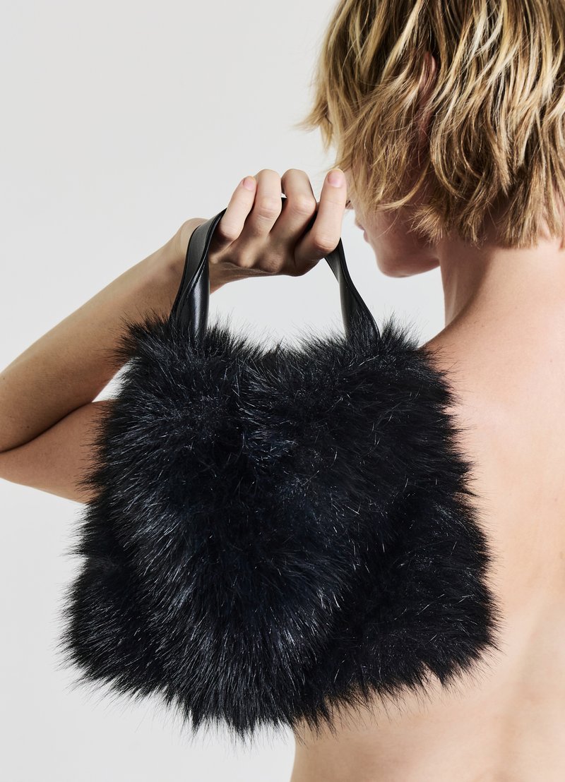 Borsa a mano in pelliccia sintetica nera con un esterno morbido e strutturato e manici in pelle nera liscia, tenuta da una persona di lato.