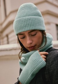 Ensemble bonnet et écharpe en maille côtelée vert menthe, avec une texture douce, un design ajusté, et des gants sans doigts assortis, idéal pour les temps frais.