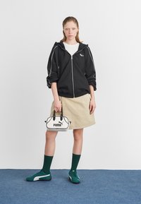 Svart zip-up hoodie med vita detaljer, beige denimkjol, gröna strumpor och teal-skor. Vit handväska med "PUMA"-logotypen synlig.