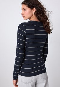 Chemise à manches longues rayée marine avec des rayures horizontales crème, texture côtelée, et un col rond, portée avec un jean gris clair.