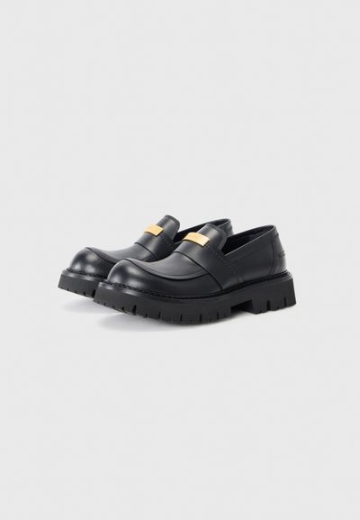Svarta läderloafers med en kraftig sula, med ett guldaccentband över framsidan. Minimalistisk design med en elegant finish.