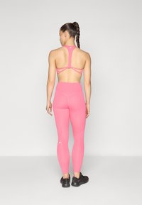 Rosa sportsbh med racerback-design og utbrettede detaljer, kombinert med matchende høy midje rosa leggings. Svarte treningssko.