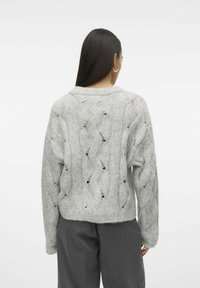 Maglione lavorato a maglia grigio chiaro con un motivo ondulato, dettagli a traforo e scollatura rotonda. Maniche lunghe e vestibilità corta.