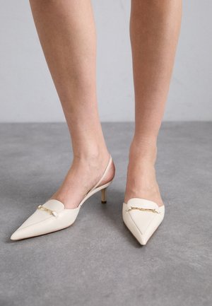 Décolleté color crema con punta affusolata e cinturino sul retro, dotate di un tacco medio sottile, caratterizzate da un accentuazione in catena dorata sulla tomaia e una texture in pelle liscia.