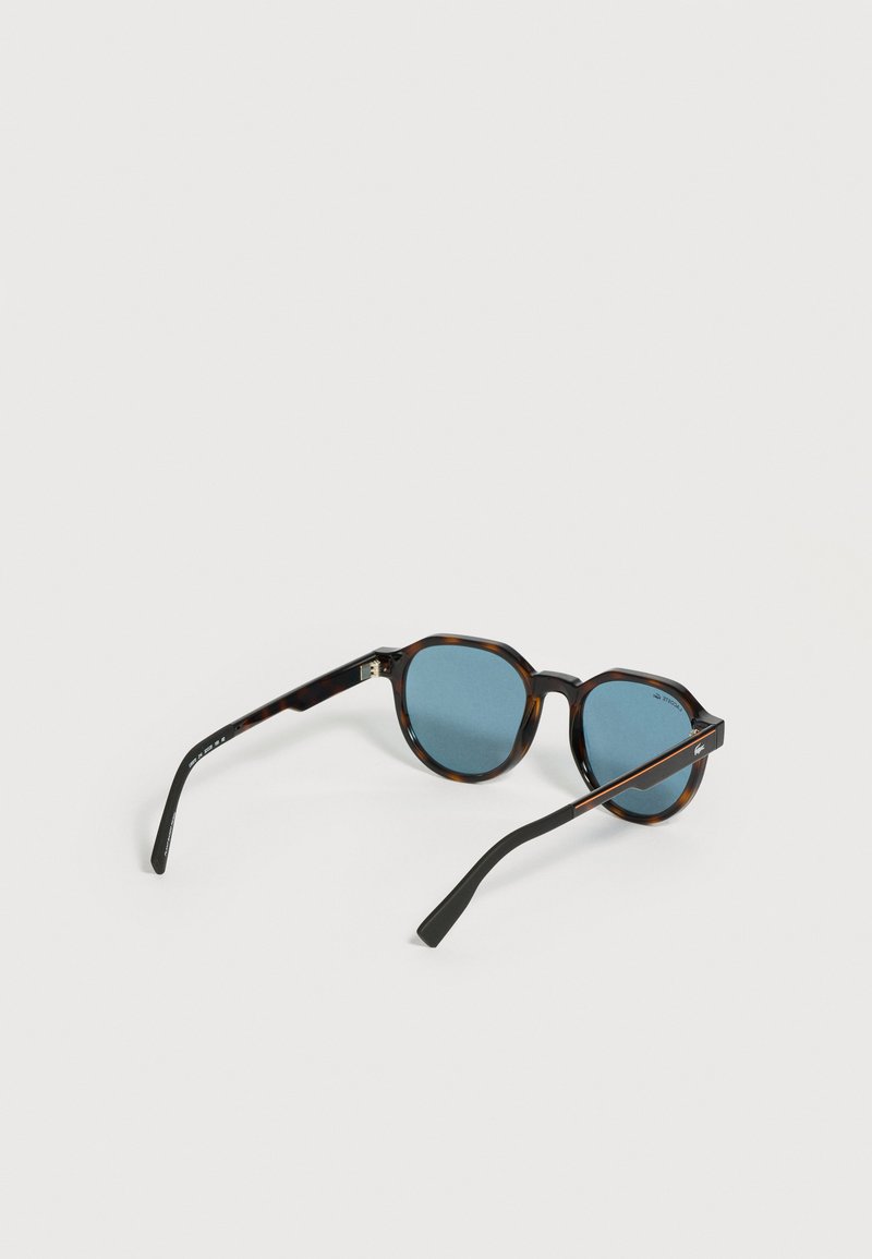 Runde Schildpatt-Sonnenbrille mit dunkelblauen Gläsern und schwarzen Bügeln, liegend auf einer weißen Oberfläche.