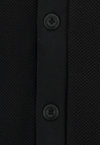 Schwarzer, texturierten Stoff mit einem gewebten Muster und einer Blende mit einem runden schwarzen Knopf, der mit "Key Largo 1994" beschriftet ist.