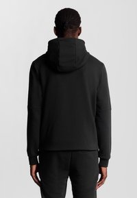 Felpa con cappuccio nera realizzata in tessuto morbido, con un ampio cappuccio regolabile, maniche lunghe e un fit rilassato, senza marchi visibili.