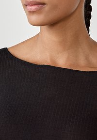 Black ribbed fabric with a wide neckline. Close-up on shoulder and neck area, showcasing a subtle texture and smooth finish.
