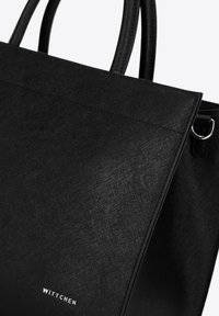 Borsa a mano sintetica nera con una texture liscia, design strutturato e doppie maniglie. Caratterizzata da dettagli del logo e da accenti di cucitura discreti.