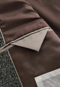 Brunt satin stof foldet over tekstureret gråt materiale, med en kontrasterende beige kant; har en trekantet flapdetalje.