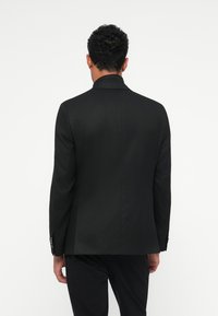 Svart kavaj med skräddarsydd passform, med en notch-lapel, strukturerade axlar och en enda bakslits. Slät yta och subtil lyster.