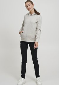 Felpa crema con un motivo testurizzato, cappuccio regolabile, due bottoni al collo e polsini a coste. Abbinata a pantaloni neri aderenti e sneakers bianche.