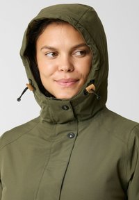 Olijfgroene jas met een hoge kraag en verstelbare capuchon, voorzien van drukknoopsluitingen en aantrekkoorden voor een veilige pasvorm. Zachte stoftextuur.