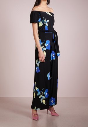 Femme portant une robe longue noire épaules dénudées avec un imprimé floral bleu et jaune et des chaussures à talons roses.