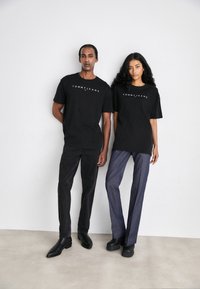 T-shirt in cotone nero con logo "TOMMY JEANS", abbinata a pantaloni scuri e calzature nere. Taglio semplice e moderno con vestibilità rilassata.