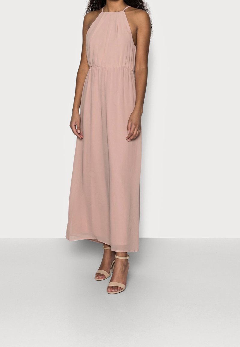 Femme portant une robe rose poudré sans manches, longue jusqu'aux chevilles, avec de fines bretelles et des sandales à talons hauts beige à bride à la cheville.
