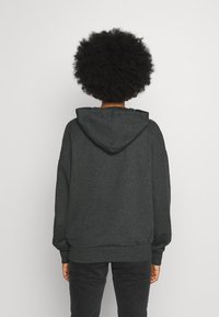 Mörkgrå huvtröja med en avslappnad passform. Har en känguruficka och ribbade muddkanter. Mjuk tygtextur, enkel design, inga mönster.