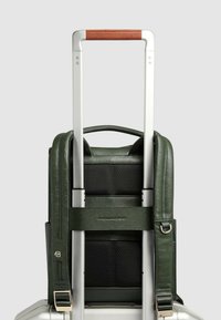 Maleta de mano de cuero verde con asa retráctil plateada, adorno de cuero marrón y correa ajustable con hebilla de tono dorado.