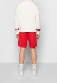 Röda shorts och en krämfärgad sweatshirt med randiga muddar. Shortsen har svarta sidopaneler, och outfiten fulländas med vita sneakers.