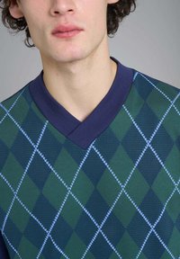 Maglione verde e blu con scollo a V, caratterizzato da un motivo a rombi argyle blu e verde scuro, con una finitura a maglia strutturata e un collare a contrasto.