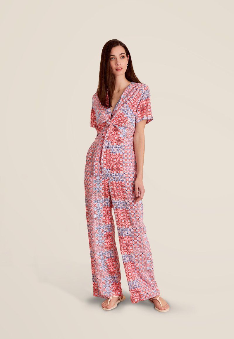 Combinaison à motifs en rouge, bleu et blanc ; manches courtes, décolleté en V profond, devant noué, coupe large, imprimés floraux et géométriques.