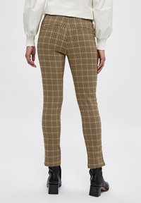 Hnědé kostkované skinny džíny s přiléhavým střihem, středním pasem a diskrétními detaily na zadních kapsách, spárované s černými kotníkovými botami.