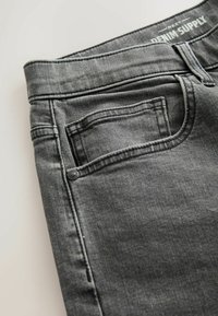 Grå denimjeans med en glat tekstur, fem-lommer design og lukning med knapper. Har diskrete syninger og mærket båndetiket i taljen.