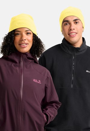 Twee mensen dragen gele mutsen en Jack Wolfskin buitenjassen, de één in paars met een capuchon, de ander in zwart fleece.