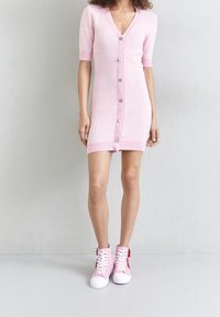 Abito rosa lavorato a maglia con maniche corte, scollo a V e dettagli con bottoni sul davanti. Abbinato a sneakers alte rosa e bianche.