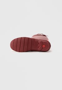 Botte en caoutchouc rouge avec semelle texturée, dotée d'une fermeture éclair sur le côté et d'une finition lisse. Motif de grip prononcé en bas pour une meilleure adhérence.