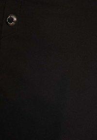 Tissu noir, texture lisse, avec un bouton en argent gravé du nom de la marque, situé sur la gauche près de la couture.