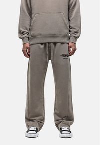 Grauer Sweatshirt und passende Hose aus weichem Material, mit einer Vordertasche und gesticktem Logodetail auf der Hose.