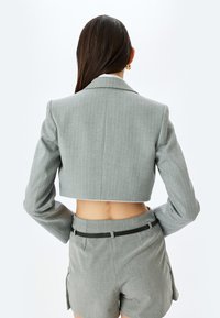 Geruite grijze blazer met verticale streepjes, brede revers en lange mouwen; gedragen met bijpassende shorts met een zwarte tailleband.