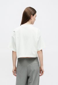 Biele krátke tričko z mäkkej bavlny s krátkymi rukávmi a zaokrúhleným výstrihom, skombinované s elegantnými sivými nohavicami s vreckom vzadu.