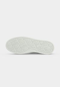 Semelle de chaussure avec motif de bande de roulement géométrique texturé et "Tommy Hilfiger" embossé près du talon, présenté sur fond blanc uni.