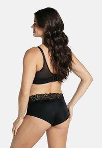 Zwarte beha en hooggeknipte slip, met een kanten tailleband. De beha heeft een gladde, doorzichtige achterkant en verstelbare banden.