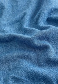 Tissu en denim de bleu moyen, présentant une surface texturée avec des motifs de tissage visibles et un léger délavage, créant une apparence douce et froissée.