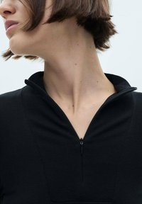 Black zip-up top with a fitted collar and textured fabric. Features a short zipper at the neck and a structured silhouette.