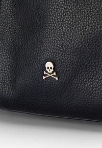 Superficie de cuero negro texturizado con un pequeño emblema de calavera y tibias cruzadas en plata, centrado cerca de la parte inferior.