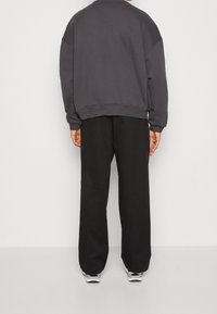 Grauer Sweatshirt mit lockerer Passform, überschnittenen Schultern und gerippten Bündchen, kombiniert mit lockeren schwarzen Hosen und Sportschuhen.