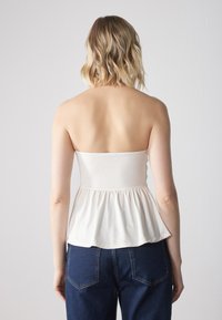 Top peplum bianco con busto aderente e orlo ampio e arricciato, abbinato a jeans blu scuro. Tessuto liscio, design senza spalline.