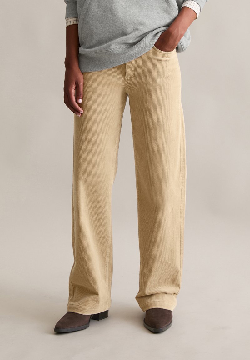 Beżowe spodnie szerokie z sztruksu o miękkiej fakturze, z bocznymi kieszeniami i luźnym krojem, zestawione z szarą bluzą z długim rękawem.